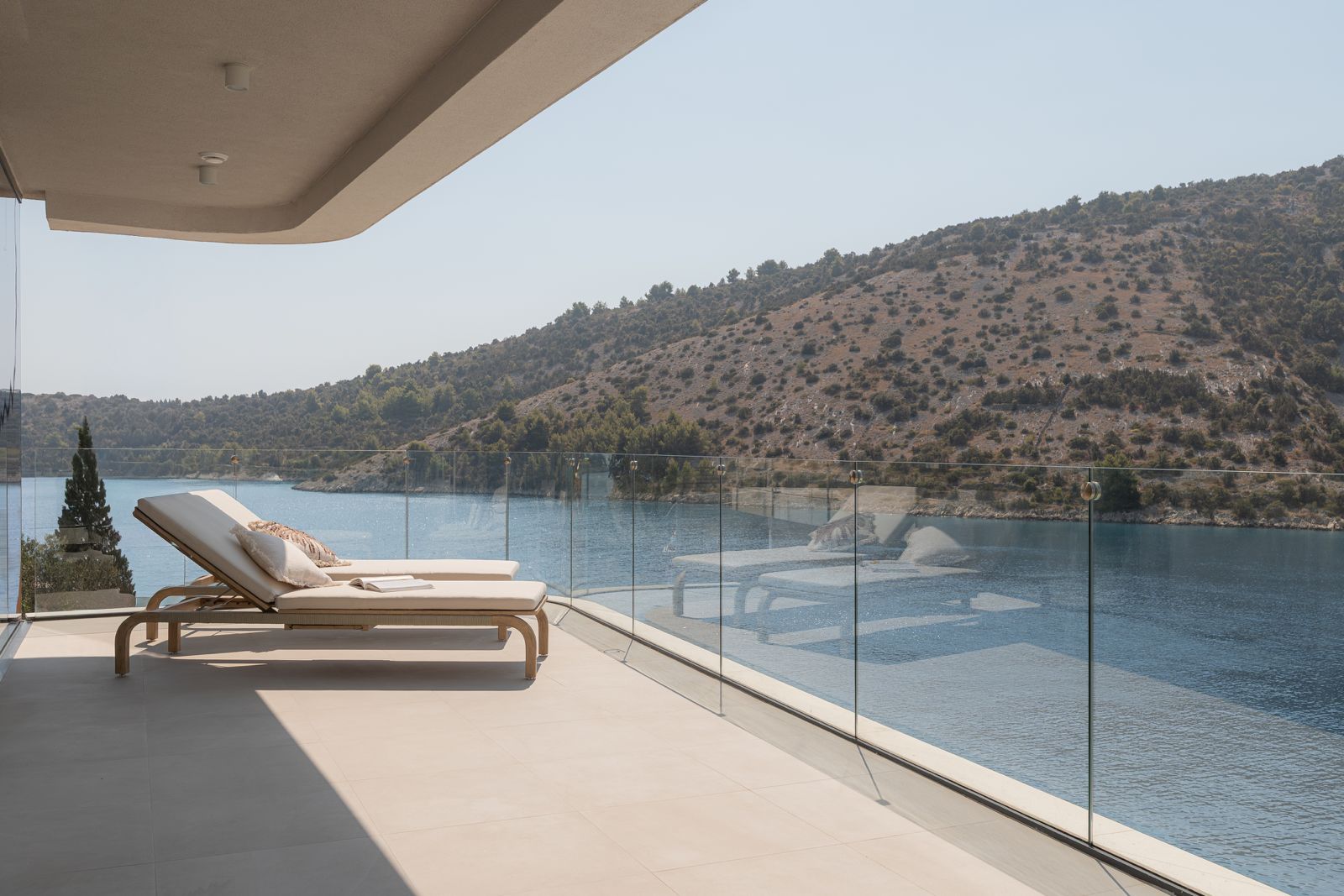 Covered sea-facing terrace with sun loungers and a glass balustrade overlooking the opposite shoreline